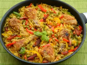 Pyszna paella z kurczakiem, ryżem, papryką i groszkiem w dużej patelni.