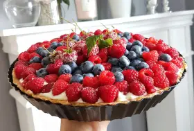 Prosta tarta z budyniem, obficie udekorowana malinami i borówkami, wygląda apetycznie.
